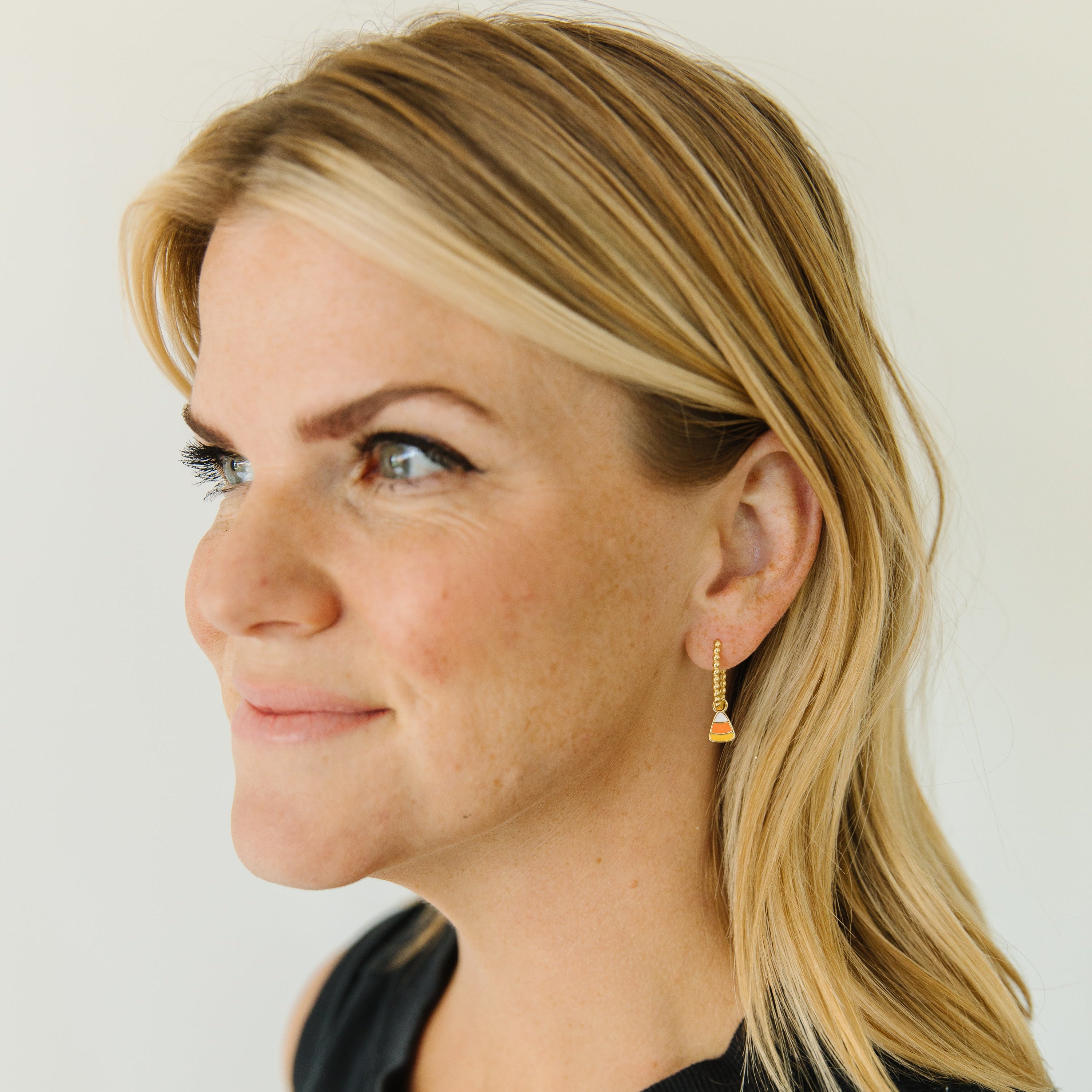 A woman with blonde hair wearing a black sleeveless top and a small gold dangle earring, shown in profile against a plain light background.