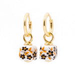 A pair of gold hoop earrings with dangling square charms featuring a white background and a black and orange floral pattern, set against a plain white background.
