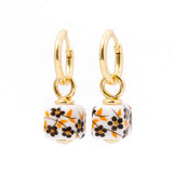 A pair of gold hoop earrings with dangling square charms featuring a white background and a black and orange floral pattern, set against a plain white background.