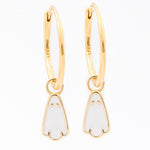 A pair of gold huggie hoop earrings with small white enamel penguin charms, shown on a plain white background.