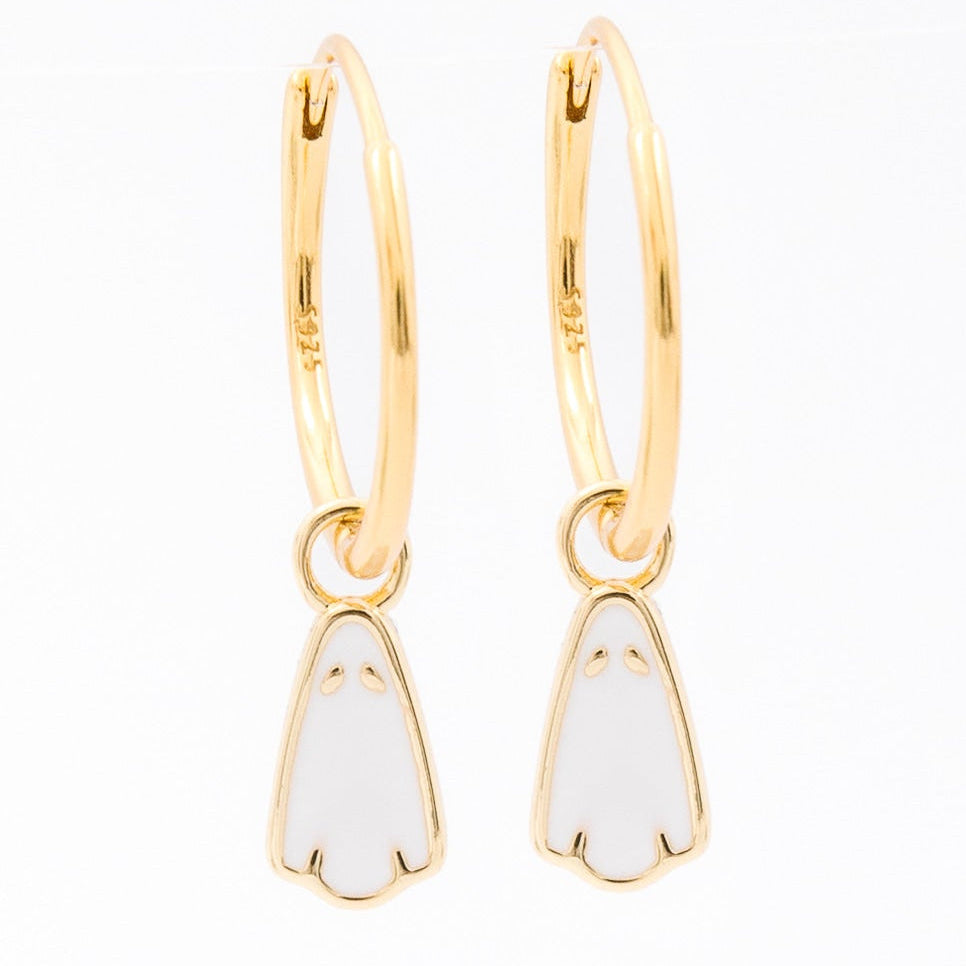 A pair of gold huggie hoop earrings with small white enamel penguin charms, shown on a plain white background.