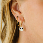 A close-up of a person's ear wearing a gold huggie hoop earring with a dangling skull charm, along with other small earrings.