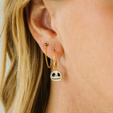A close-up of a person's ear wearing a gold huggie hoop earring with a dangling skull charm, along with other small earrings.