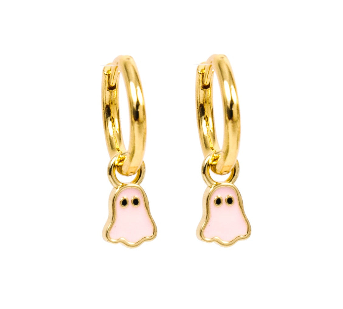 A pair of gold huggie hoop earrings with dangling ghost charms filled with light pink enamel, shown on a plain white background.
