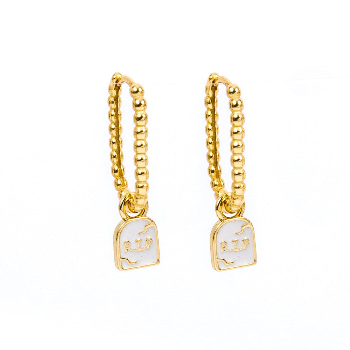 A pair of gold huggie hoop earrings with a small white enamel pendant featuring a tombstone with RIP on a plain white background.