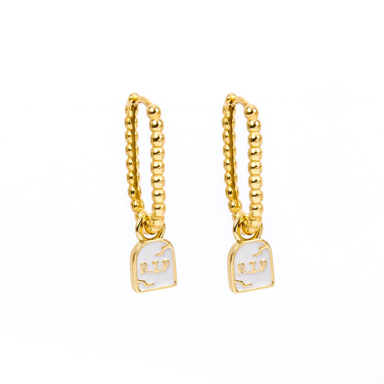 A pair of gold huggie hoop earrings with a small white enamel pendant of a tombstone that says RIP on a plain white background.
