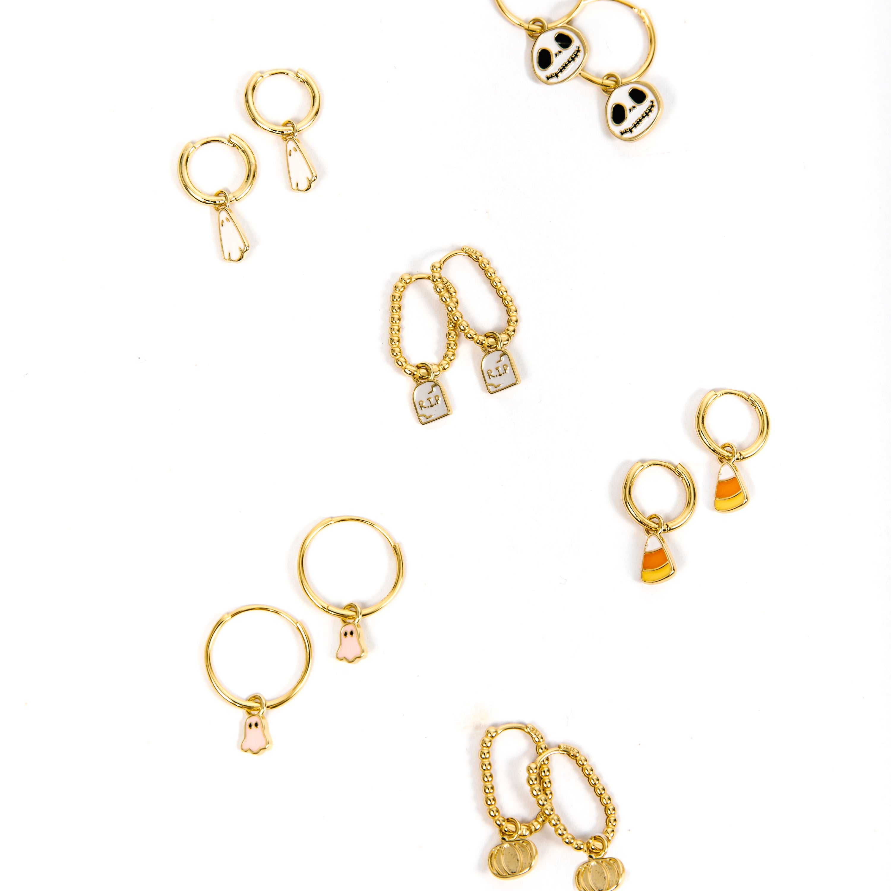 Six pairs of gold hoop earrings with various charms, including Jack Skellington, candy corn, tombstone, pink ghosts, white ghosts, and gold pumpkins, arranged on a plain white background.