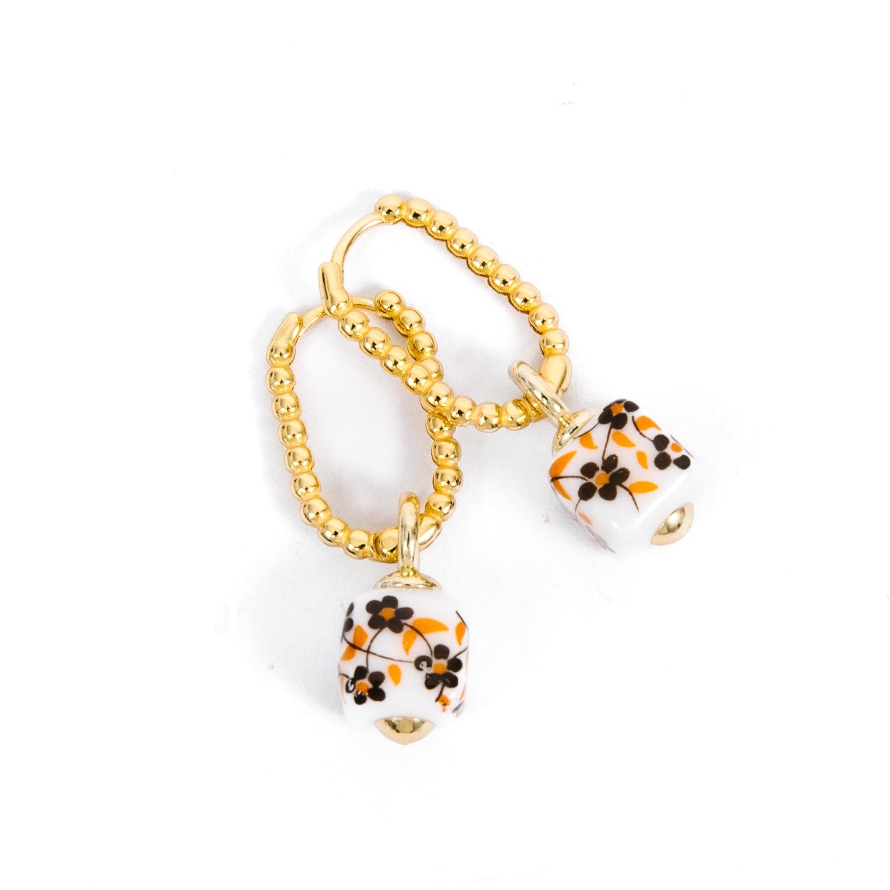 A pair of gold chain earrings with dangling white beads decorated with orange and black floral patterns, set against a plain white background.
