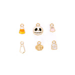 Six small gold-tone Halloween-themed charms arranged on a white background, including a candy corn, skull, pink ghost, white ghost, gold pumpkin, and white tombstone.