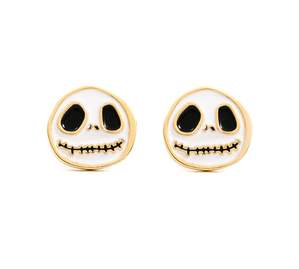 A pair of skull-shaped stud earrings with a white enamel face, black eyes and mouth details, and a gold-tone border, shown on a plain white background.