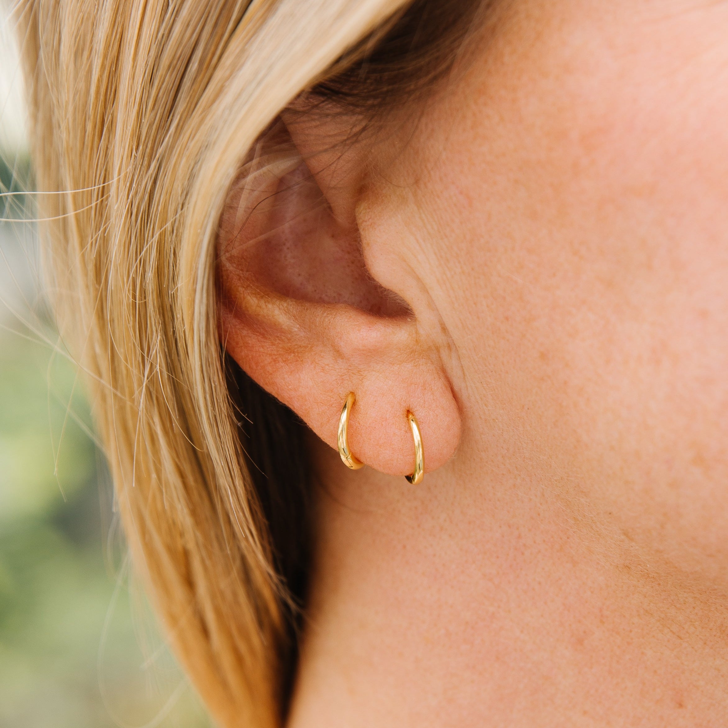 Close-up of a person wearing gold hoop earrings with a blurred background