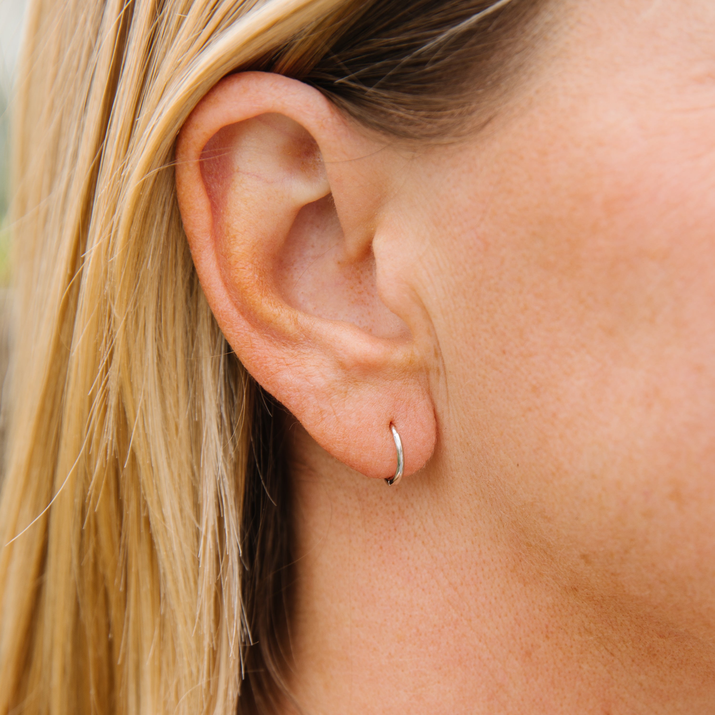 Close-up of a person wearing a small silver hoop earring with blonde hair.